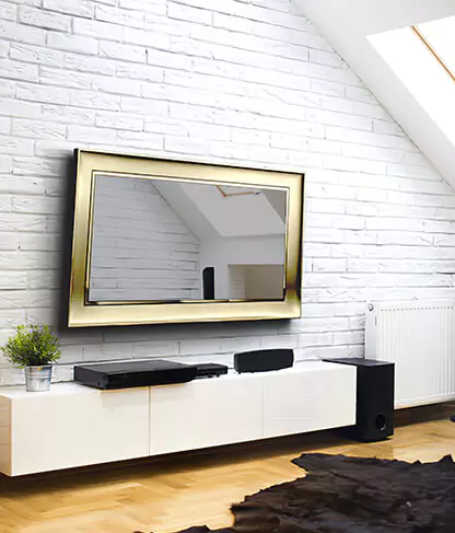 A gold framed mirror TV is mounted on a white brick wall above a sideboard cabinet.