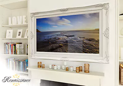 White framed smart mirror TV on a plain wall with book shelves on the side and gold voltives.